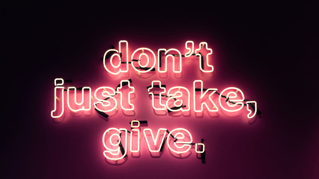 A pink sign light in the dark and says" don't just take, give."