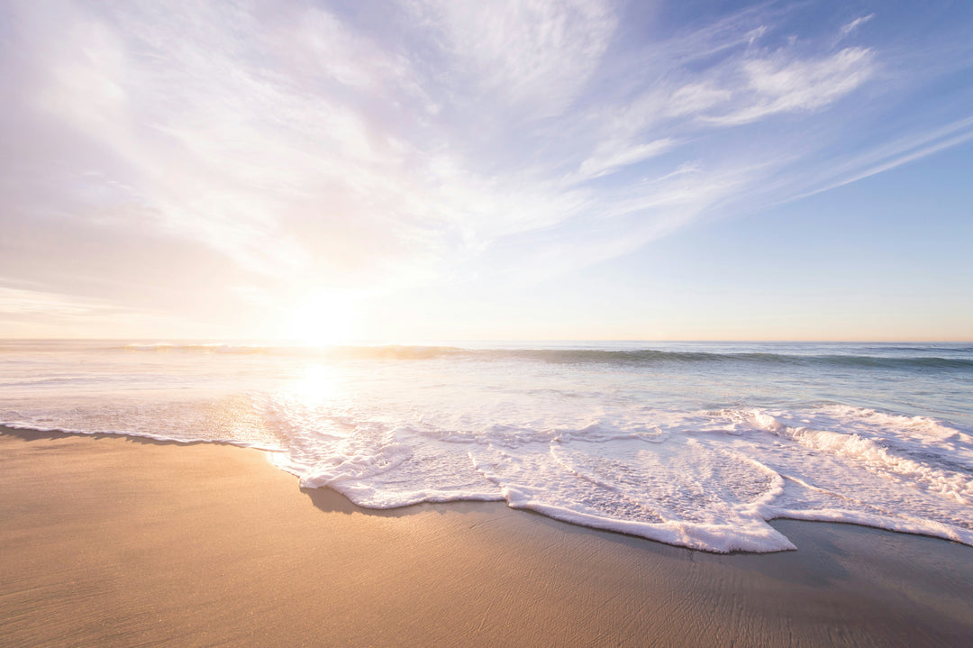 A serene beach scene at sunrise or sunset, with gentle ocean waves washing onto the sandy shore.