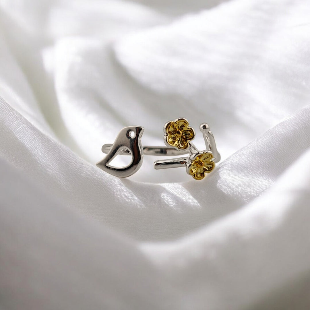 Silver ring with two gold-plated flowers resting on soft white fabric

