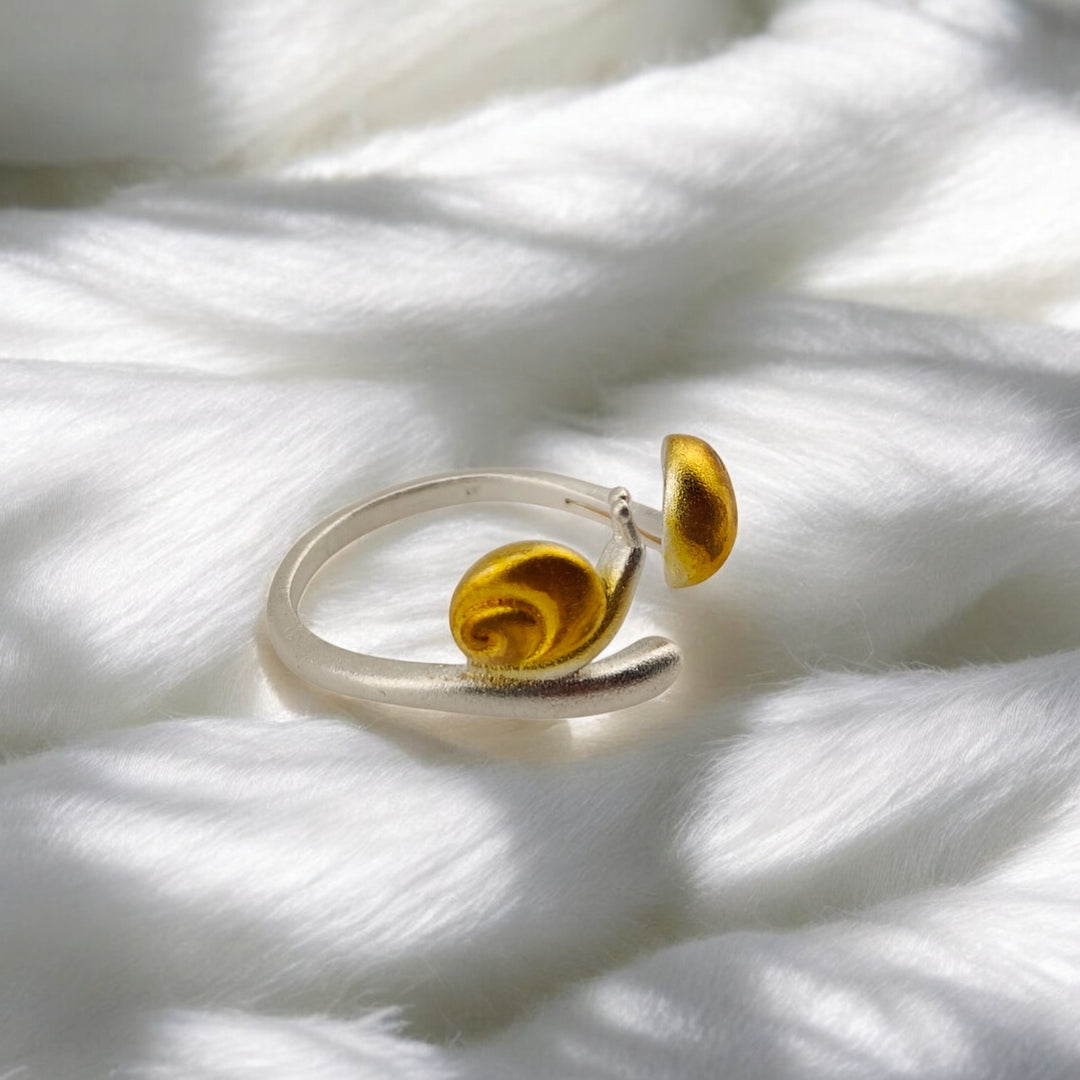 Side view of silver snail ring with golden enamel shell on soft background

