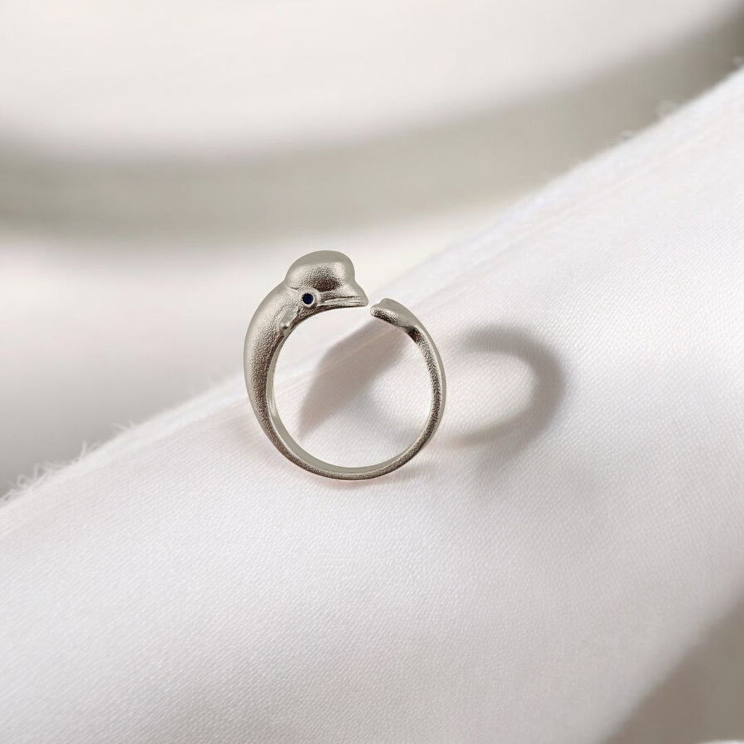 Matte silver dolphin-shaped ring resting on soft white fabric