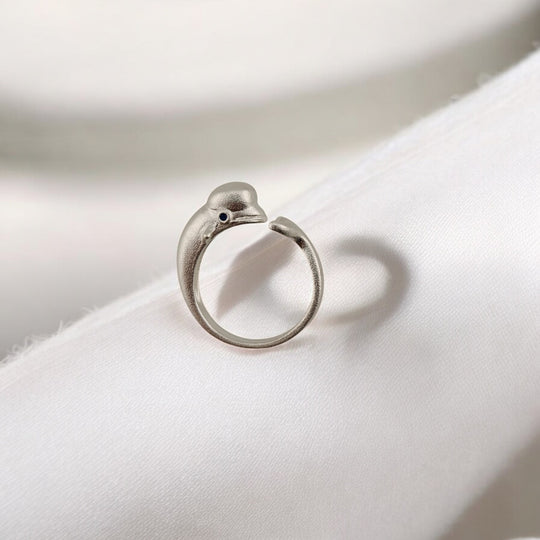 Matte silver dolphin-shaped ring resting on soft white fabric