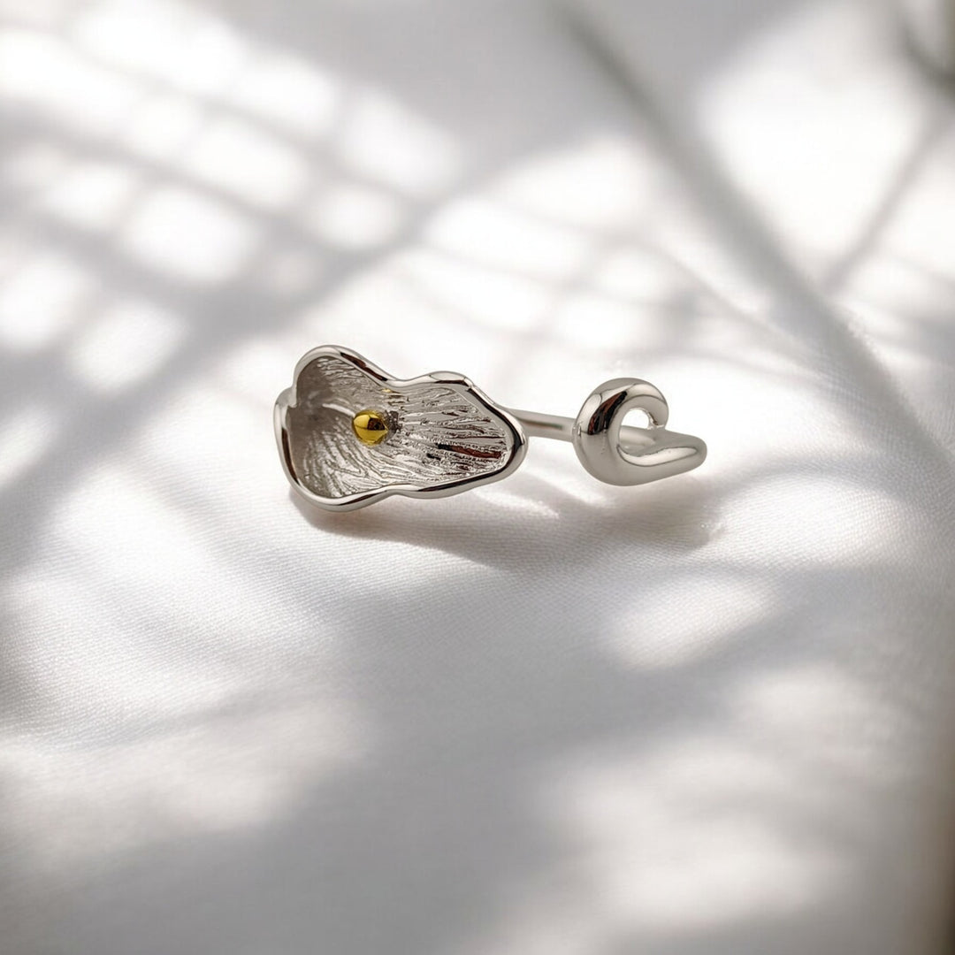 Silver calla lily ring with gold center resting on white fabric with soft shadows