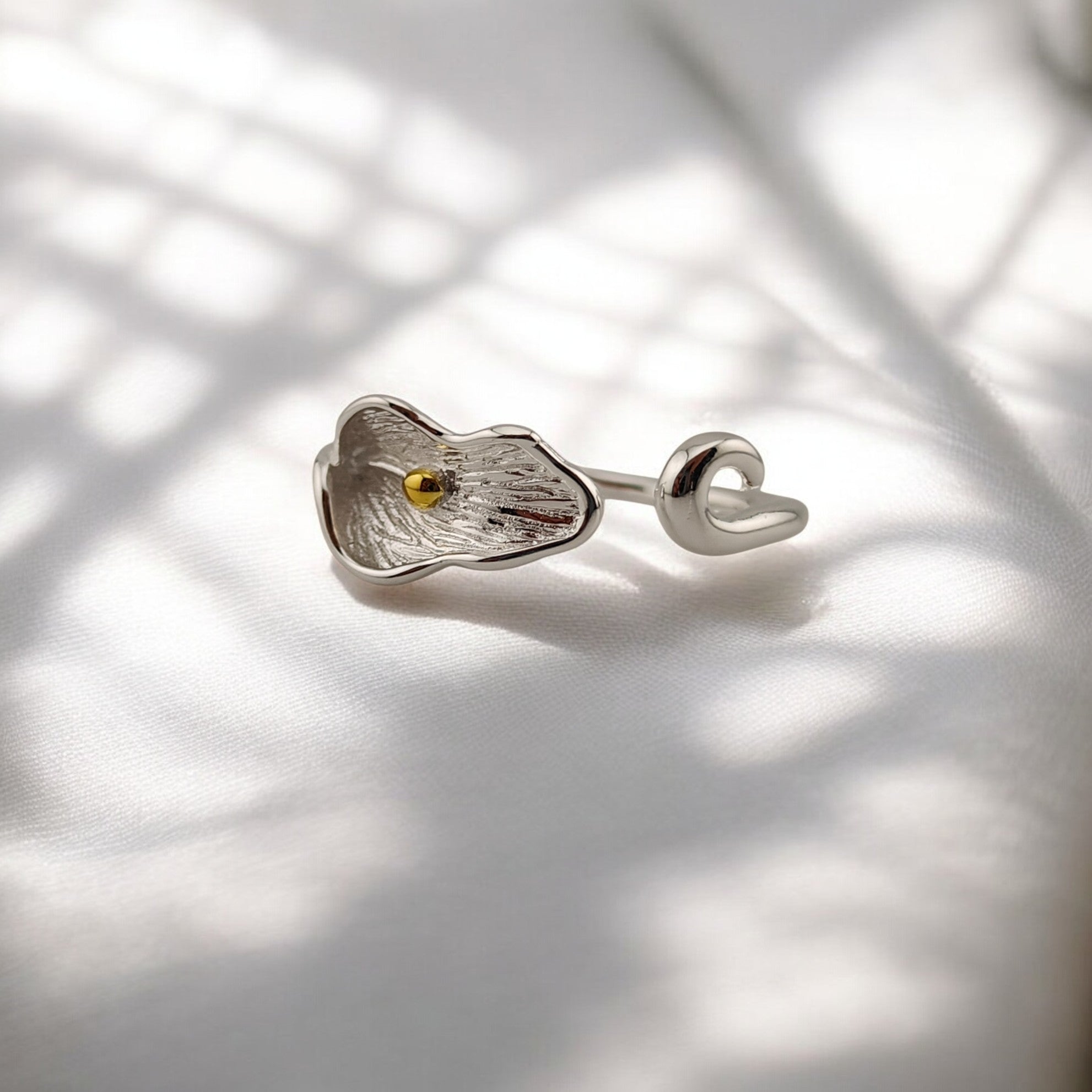 Silver calla lily ring with gold center resting on white fabric with soft shadows