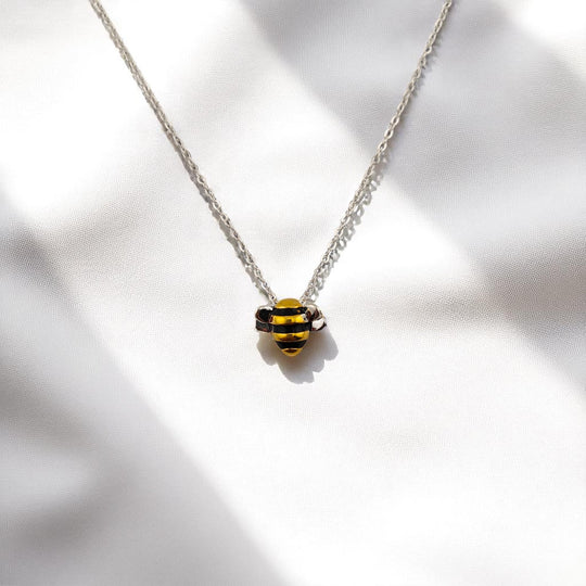 Bee pendant necklace displayed with chain on marble and fabric