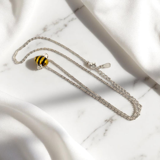 Side view of bee necklace resting softly on white satin