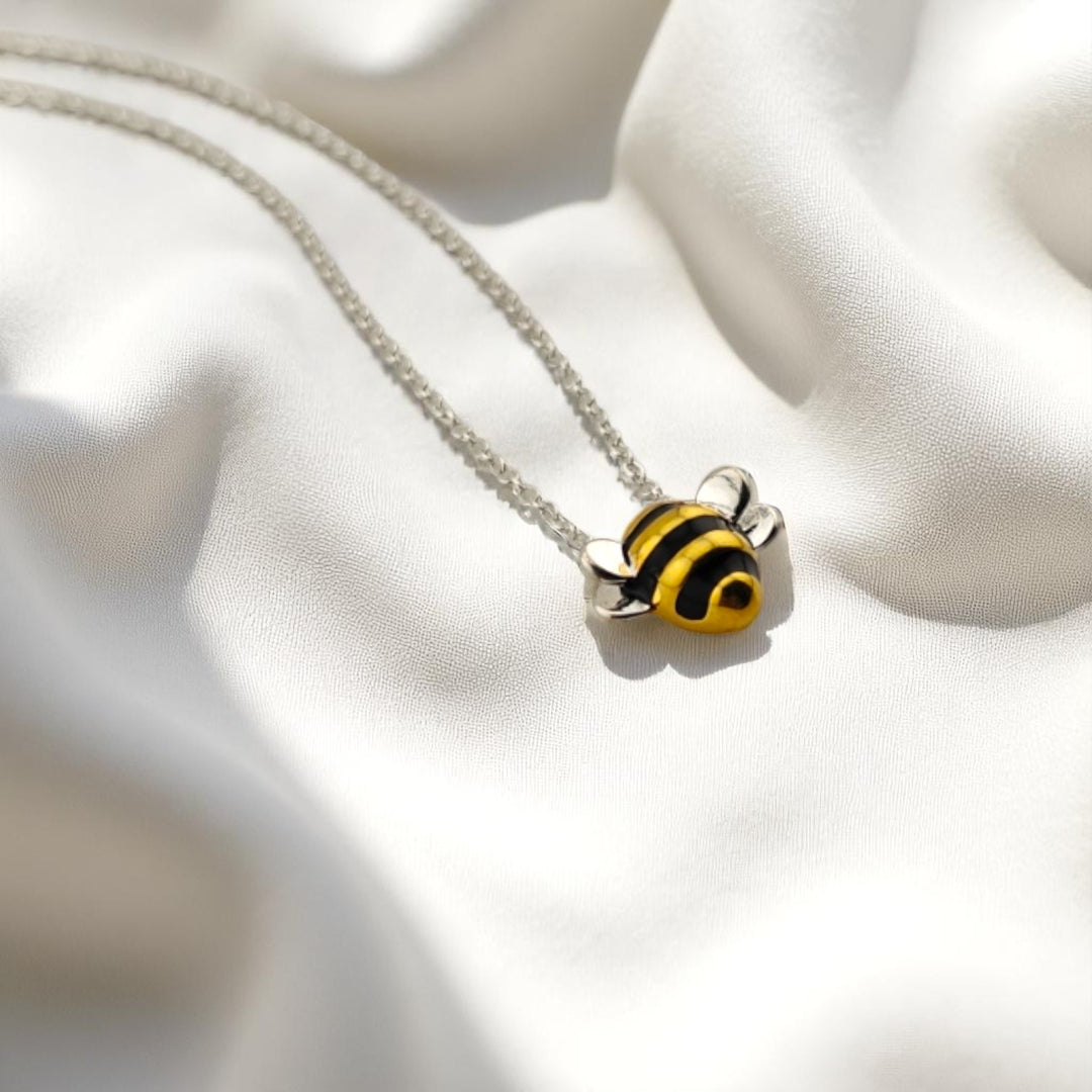 Silver necklace with yellow and black bee pendant on white fabric