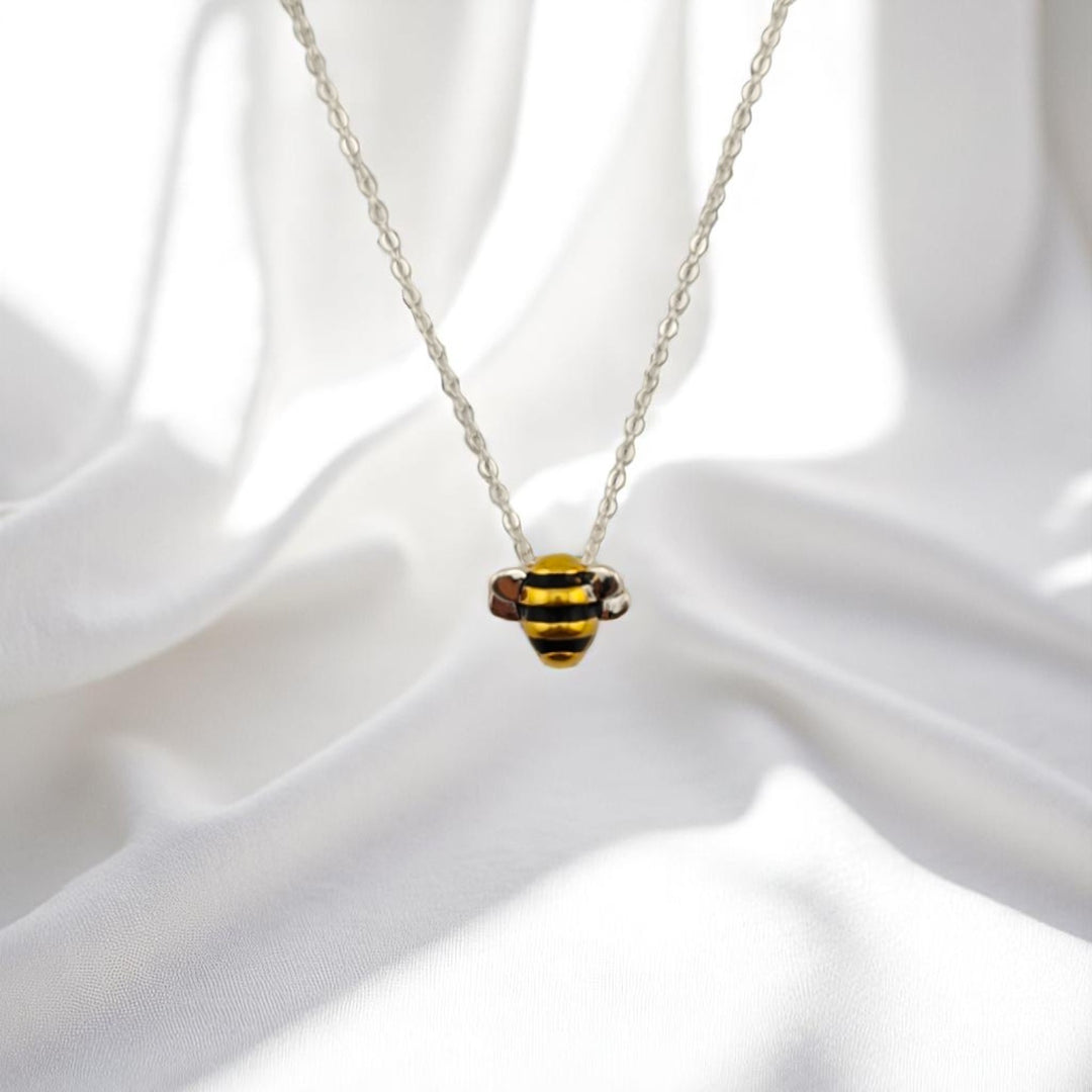 Close-up of enamel bee charm necklace lying on white background