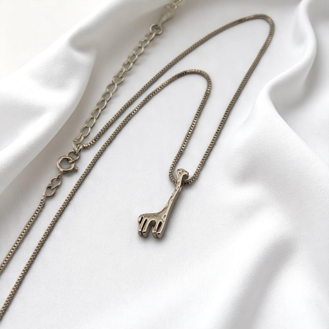 Silver necklace with minimalist giraffe pendant on white satin