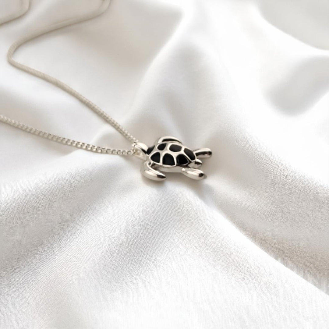 Silver sea turtle necklace with black shell pendant – close-up on satin background
