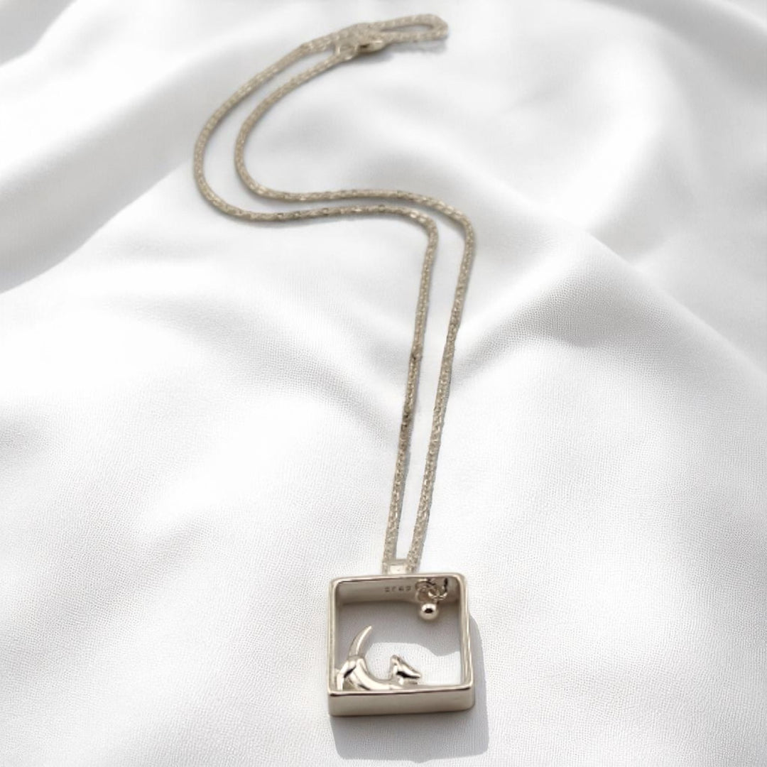Silver dog pendant necklace lying flat on smooth satin