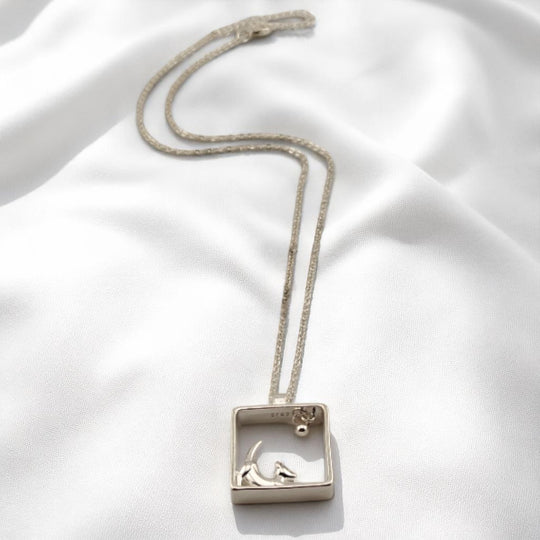 Silver dog pendant necklace lying flat on smooth satin