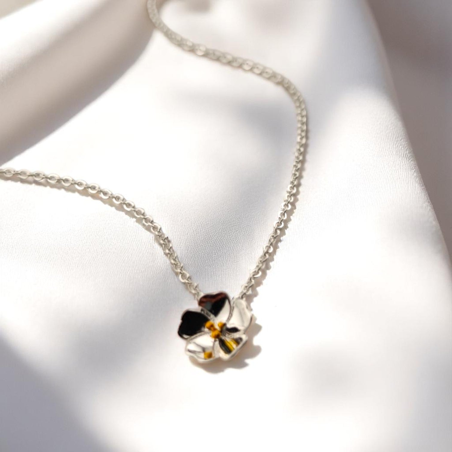 Eco-conscious pansy pendant necklace resting on bright white fabric