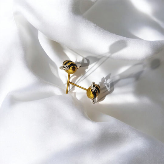Bee earrings resting on white fabric with light and shadow play