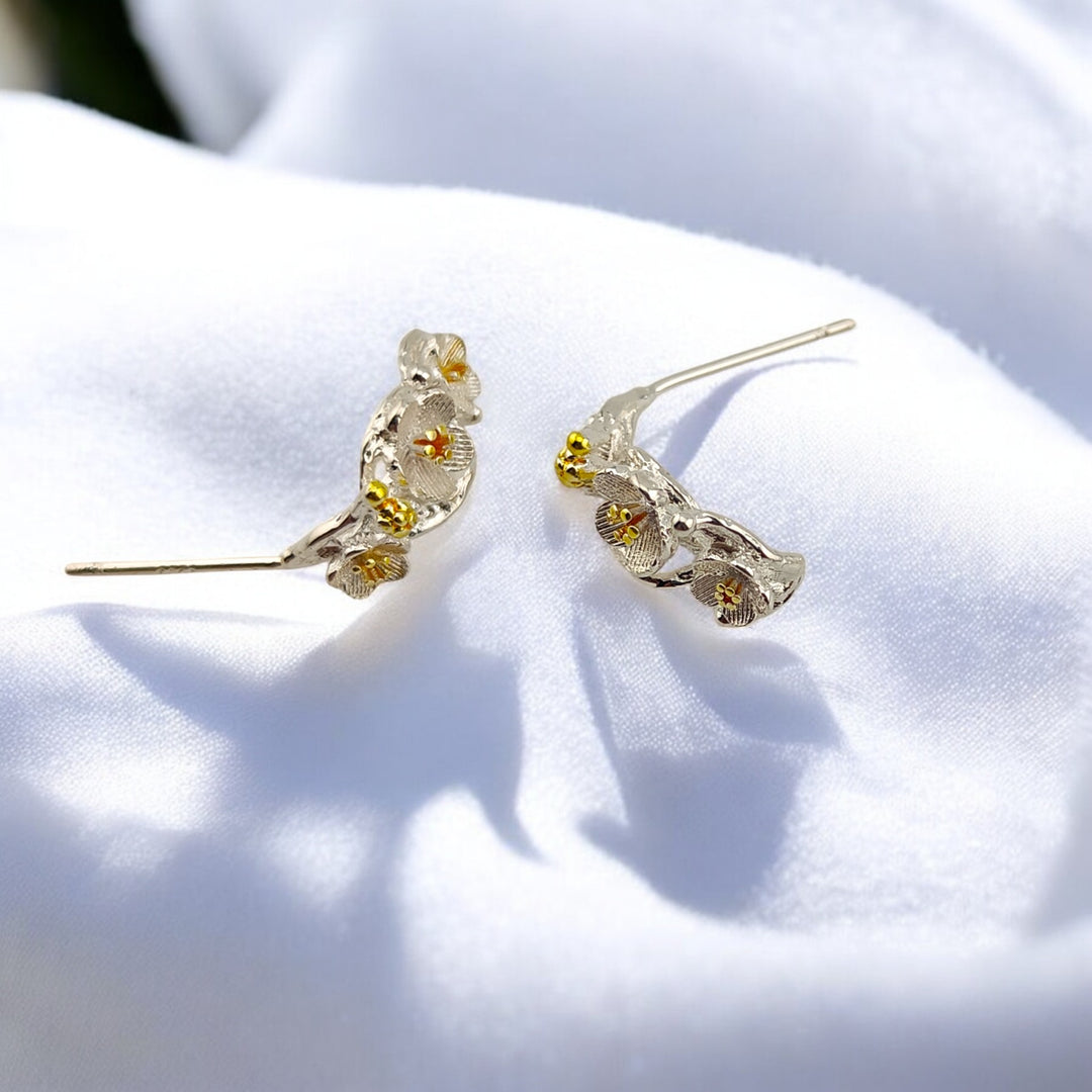 Pair of silver floral climber earrings lying flat under soft sunlight
