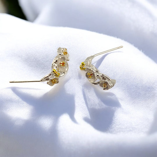 Pair of silver floral climber earrings lying flat under soft sunlight