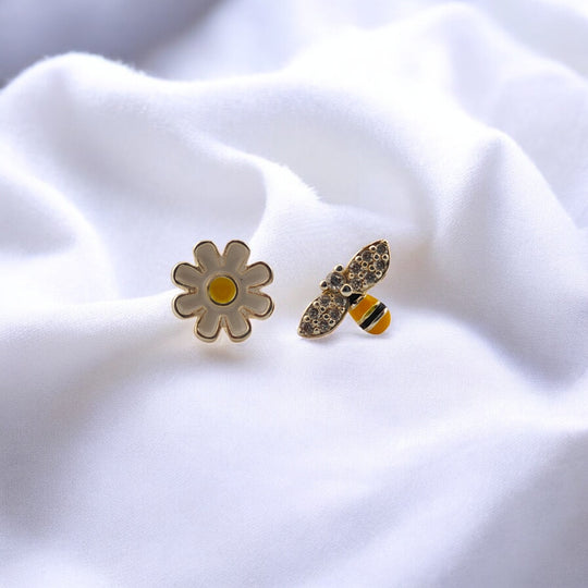 Close-up of mismatched daisy and bee stud earrings on white fabric

