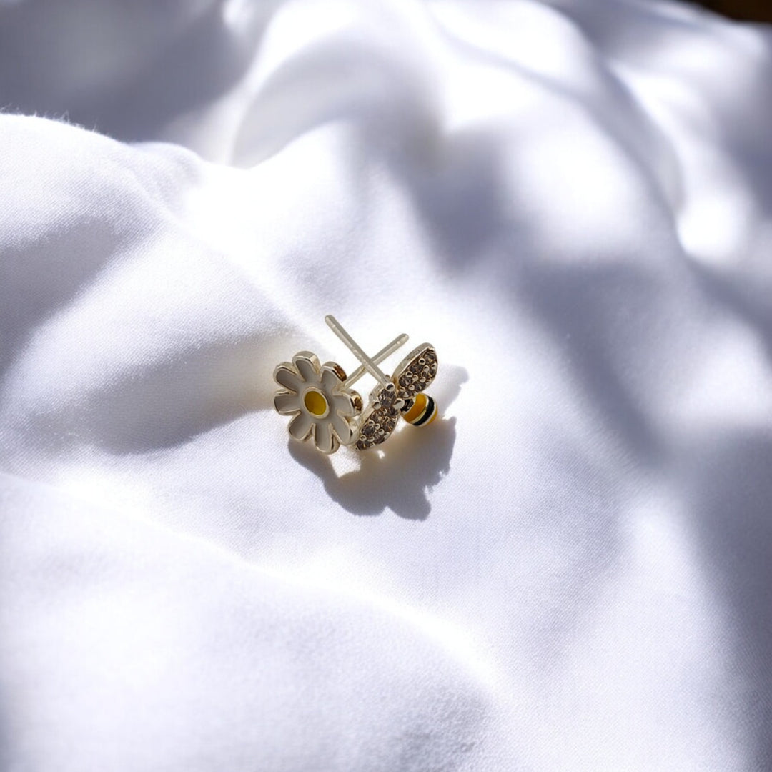 Bee earring beside yellow flower on soft fabric

