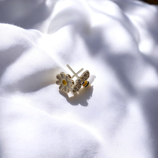 Bee earring beside yellow flower on soft fabric

