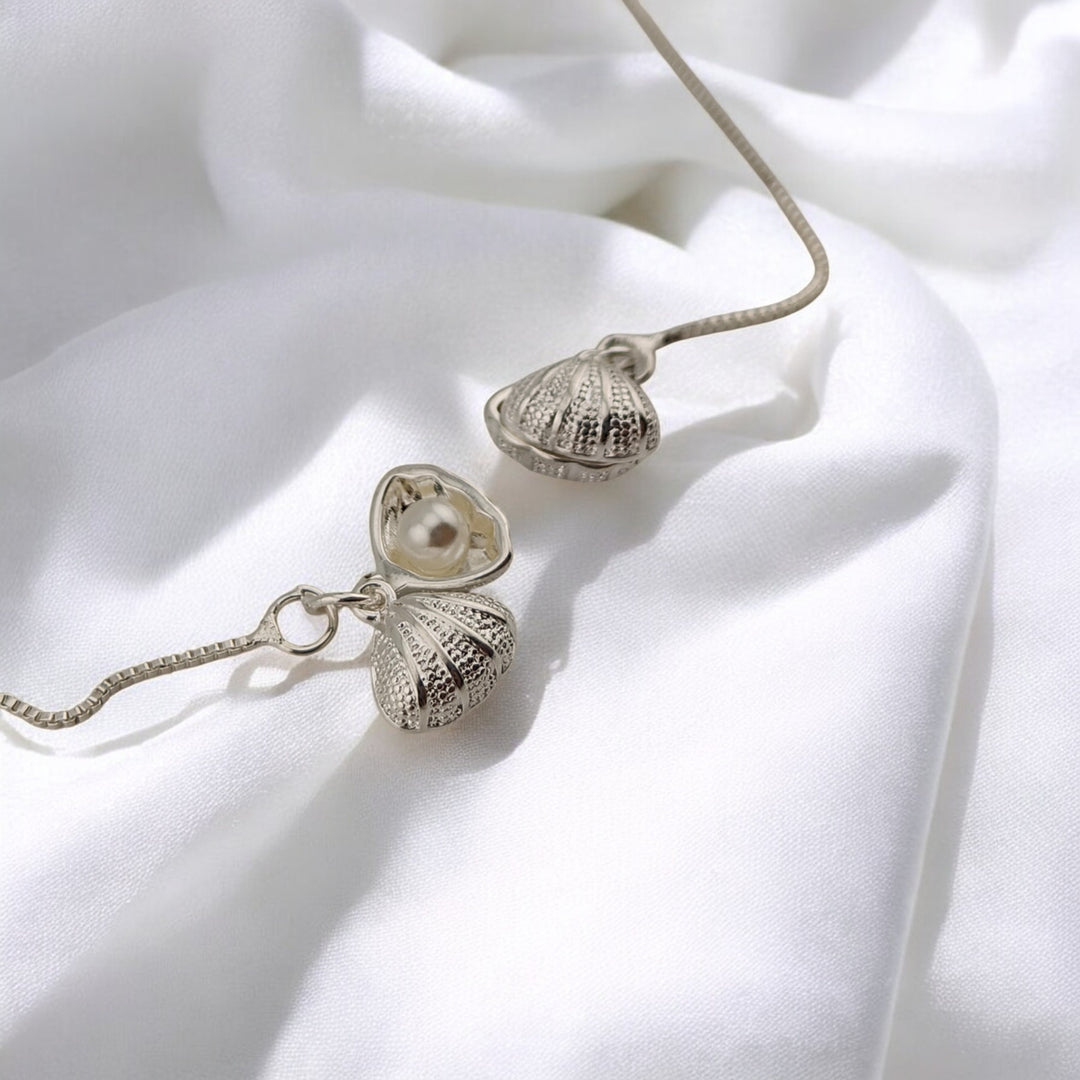 Close-up of silver seashell earrings with open shell and pearl inside