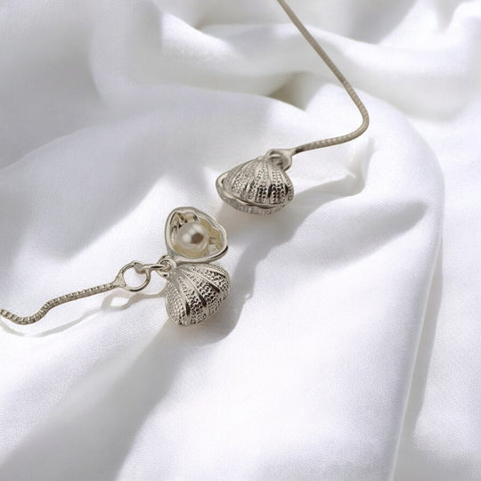 Close-up of silver seashell earrings with open shell and pearl inside