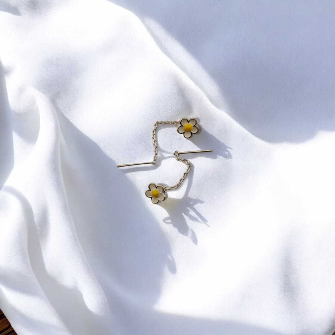 
Elegant gold-tone threader earrings with double white blossoms and yellow centers, resting on white fabric.