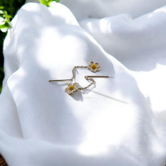 Lightweight floral earrings featuring daisy motifs on a fine chain, captured in bright natural daylight.