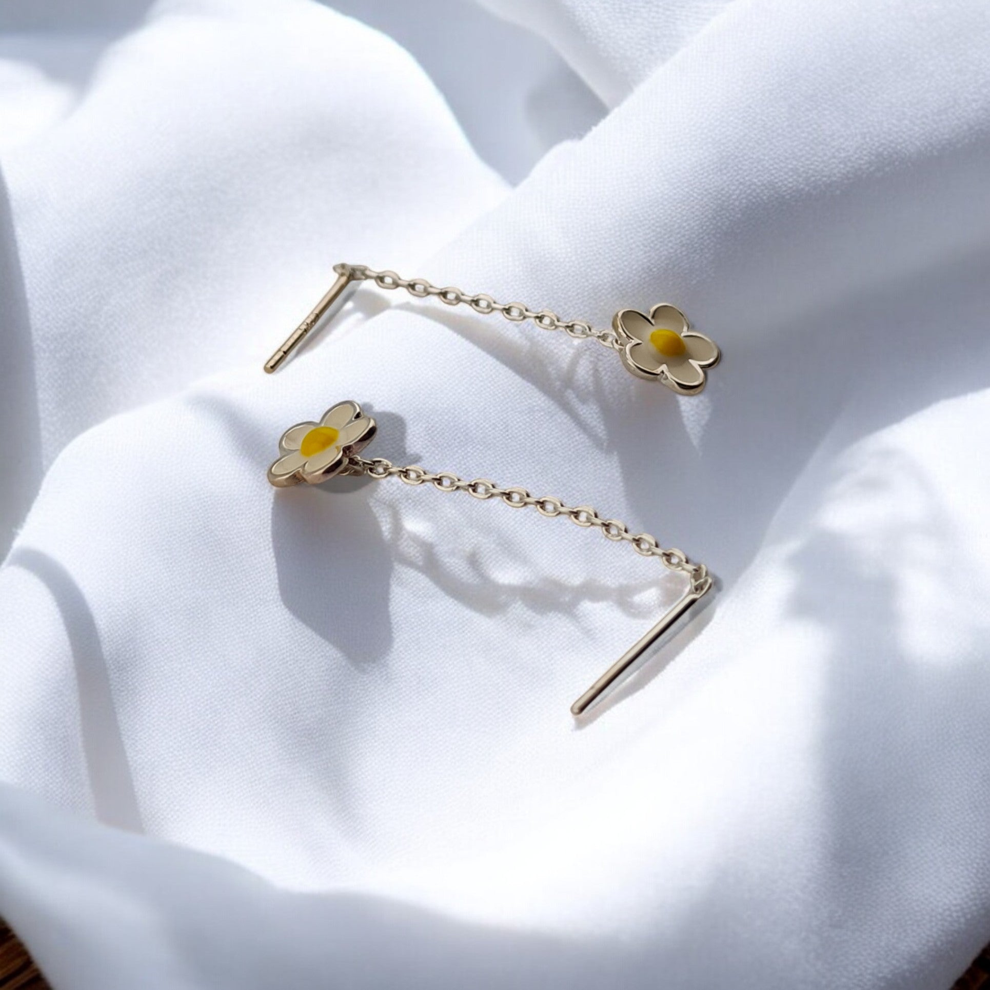 Close-up of floral chain earrings with yellow center detail, laid out on soft white satin.