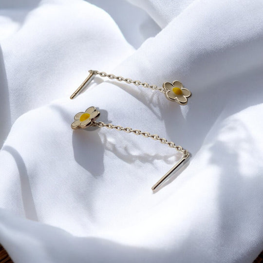Close-up of floral chain earrings with yellow center detail, laid out on soft white satin.