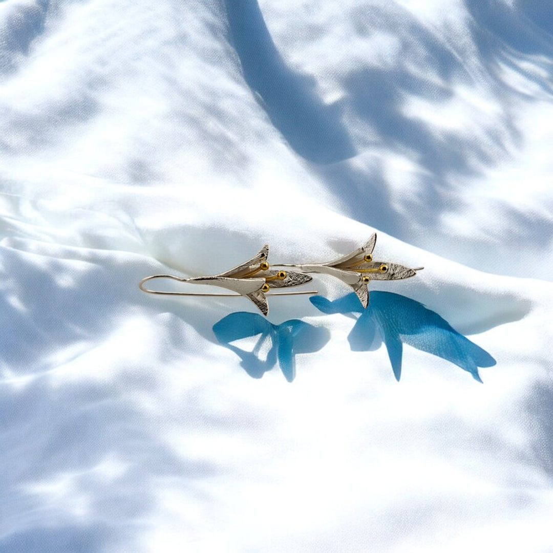 Pair of silver and gold lily threader earrings on white fabric background