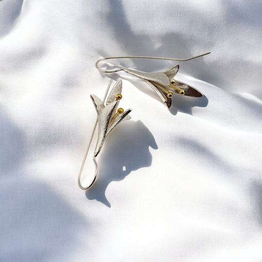 Close-up of silver floral drop earrings with golden bead accents, flat-lay style