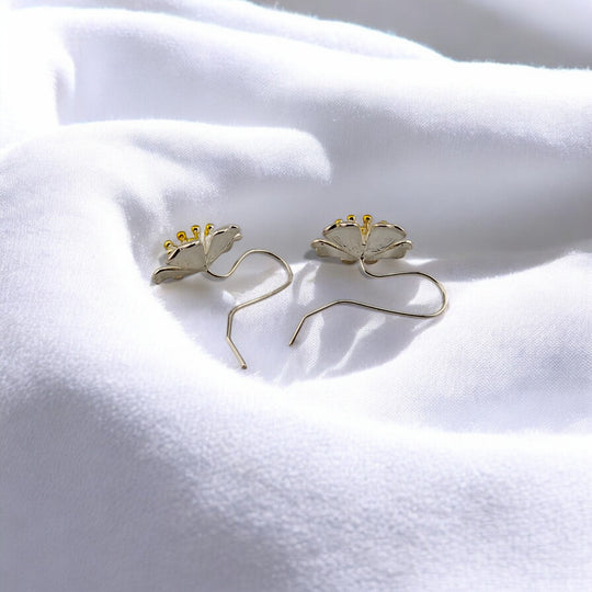 Back view of silver floral hook earrings with golden flower centers lying on white fabric