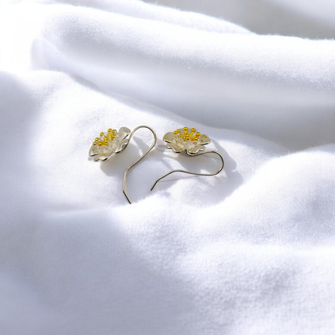 Side view of flower-shaped silver earrings with detailed golden stamens, displayed on soft fabric