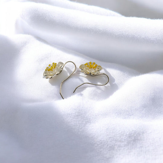 Side view of flower-shaped silver earrings with detailed golden stamens, displayed on soft fabric