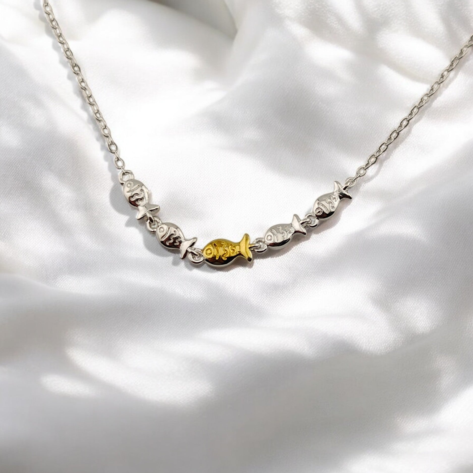 Close-up of silver bracelet with central golden fish charm on white fabric

