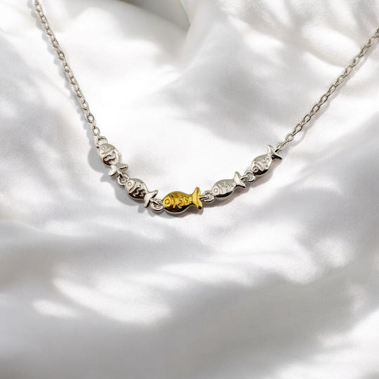 Close-up of silver bracelet with central golden fish charm on white fabric

