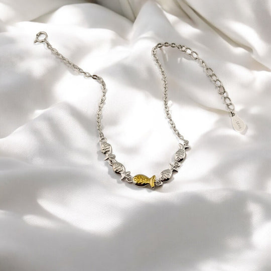 Top view of eco-friendly fish-themed bracelet with one gold fish among silver ones


