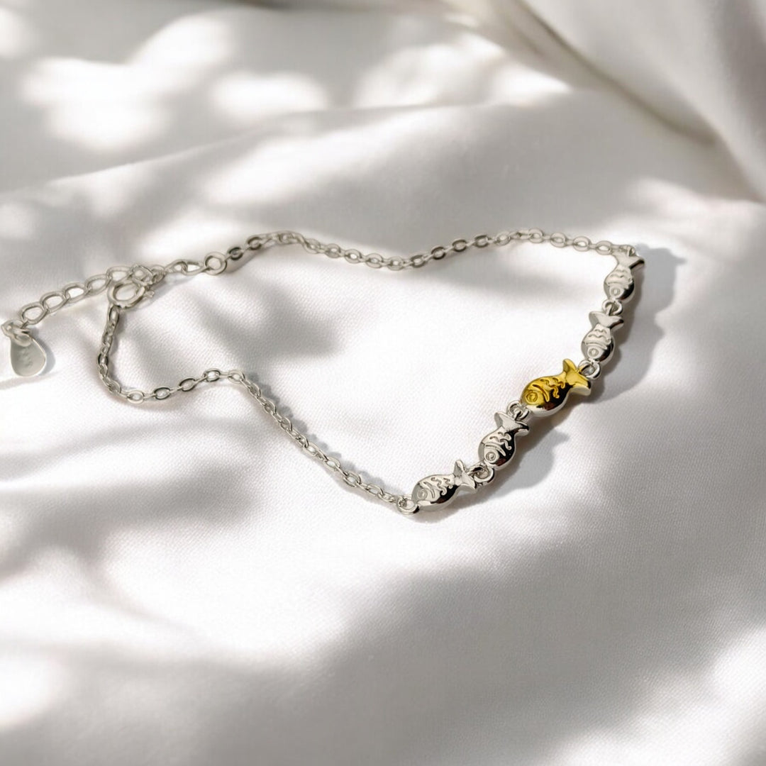 Artistic photo of bracelet chain with fish design and gold accent in center

