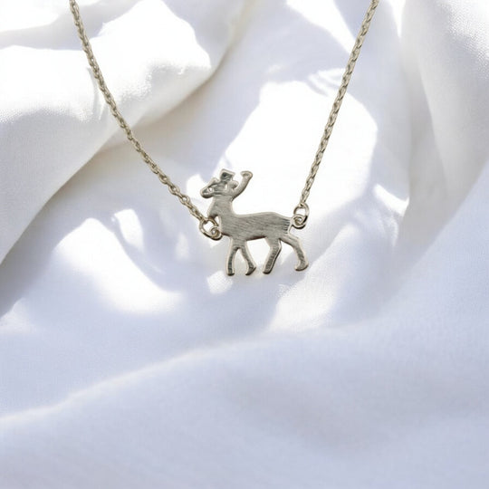 Close-up of a silver reindeer charm bracelet from RossJewelrys, resting on soft white fabric in natural light.

