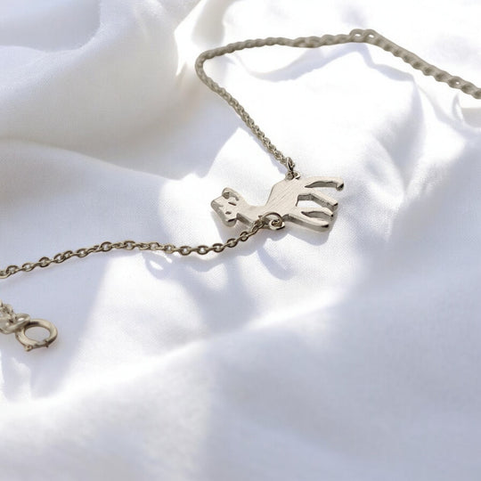 Top view of the RossJewelrys reindeer bracelet displayed open on white satin, with visible extension chain and charm.

