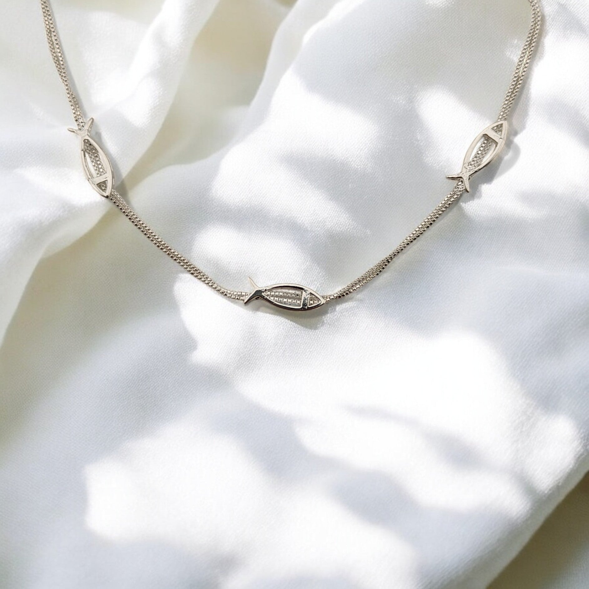Elegant silver bracelet with fish charms, partially curled on fabric