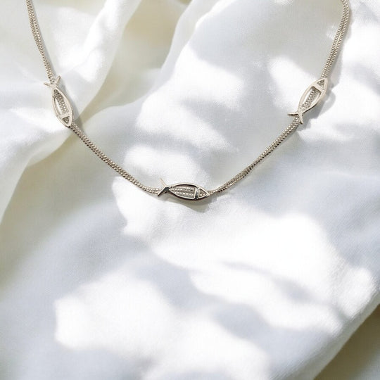 Elegant silver bracelet with fish charms, partially curled on fabric