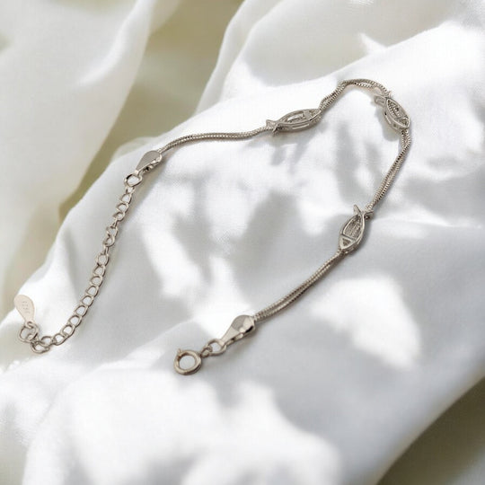 Double-chain fish design bracelet in silver, laying gently on white cloth