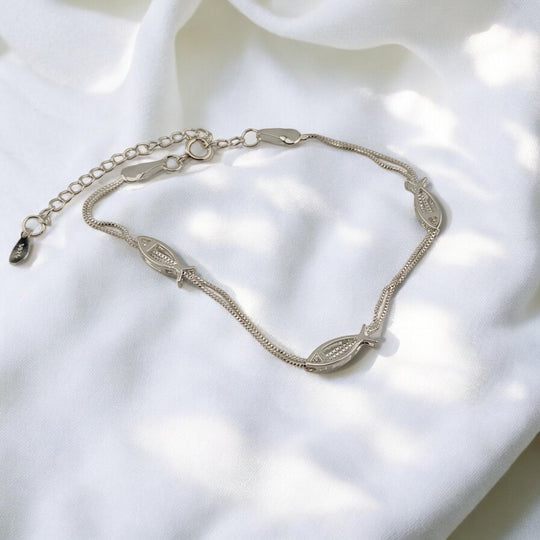 Silver fish bracelet laid flat on white fabric with soft shadows