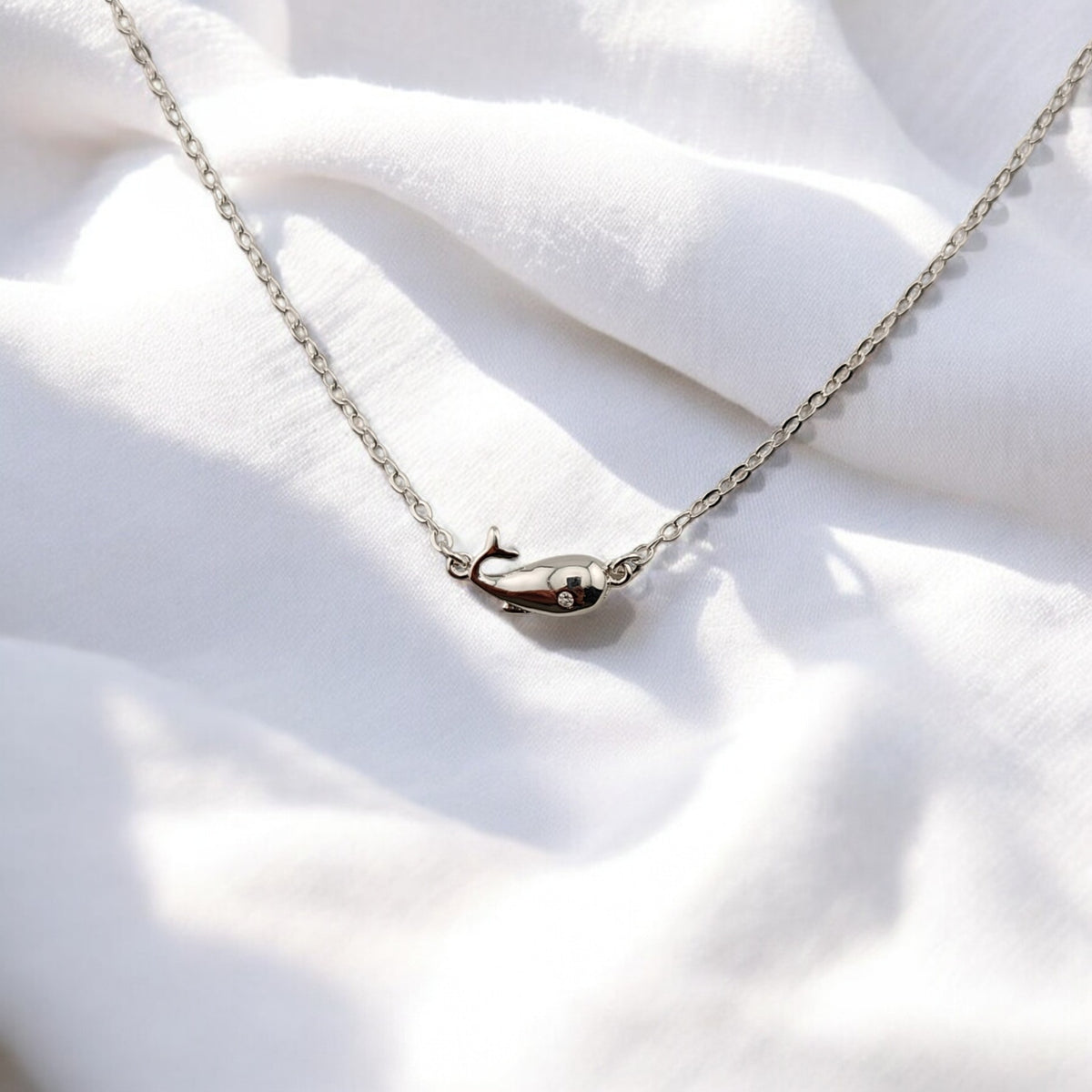 Close-up of whale-shaped silver charm in bracelet on soft white fabric