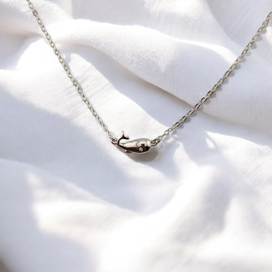 Close-up of whale-shaped silver charm in bracelet on soft white fabric