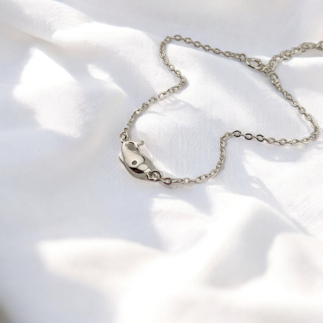 Silver whale charm bracelet lying on white fabric background