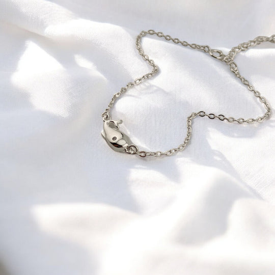 Silver whale charm bracelet lying on white fabric background