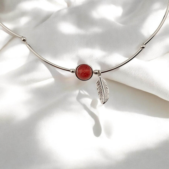 Close-up of red gemstone and feather charm on elegant silver bracelet