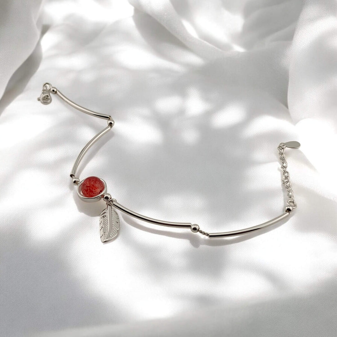 Open silver bracelet with red center charm and feather accent